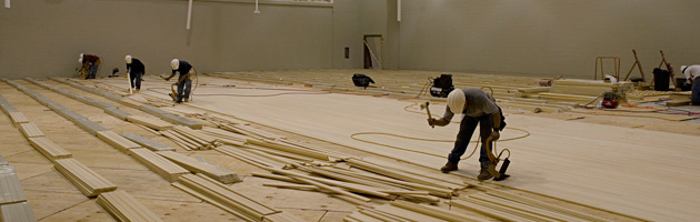 A line of workers in a gym installing a new bamboo multisport flooring system.